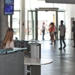 A bustling office reception area with people walking and a receptionist at a modern desk.